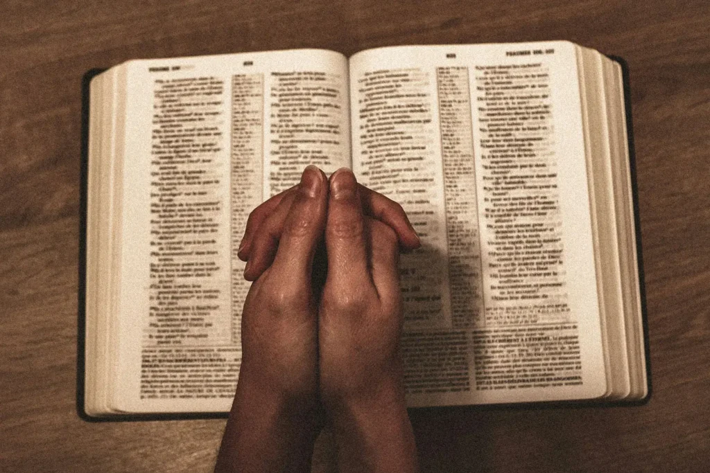 praying hands on top of an open bible