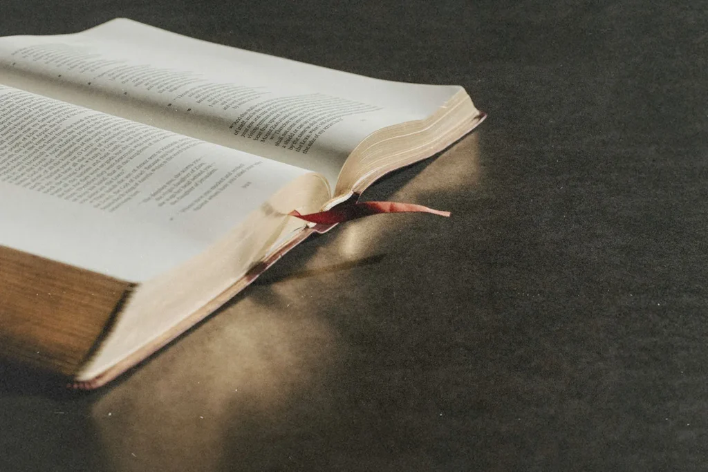 Open Bible lies on a dark surface, its pages slightly curved with a ribbon bookmark extending outward