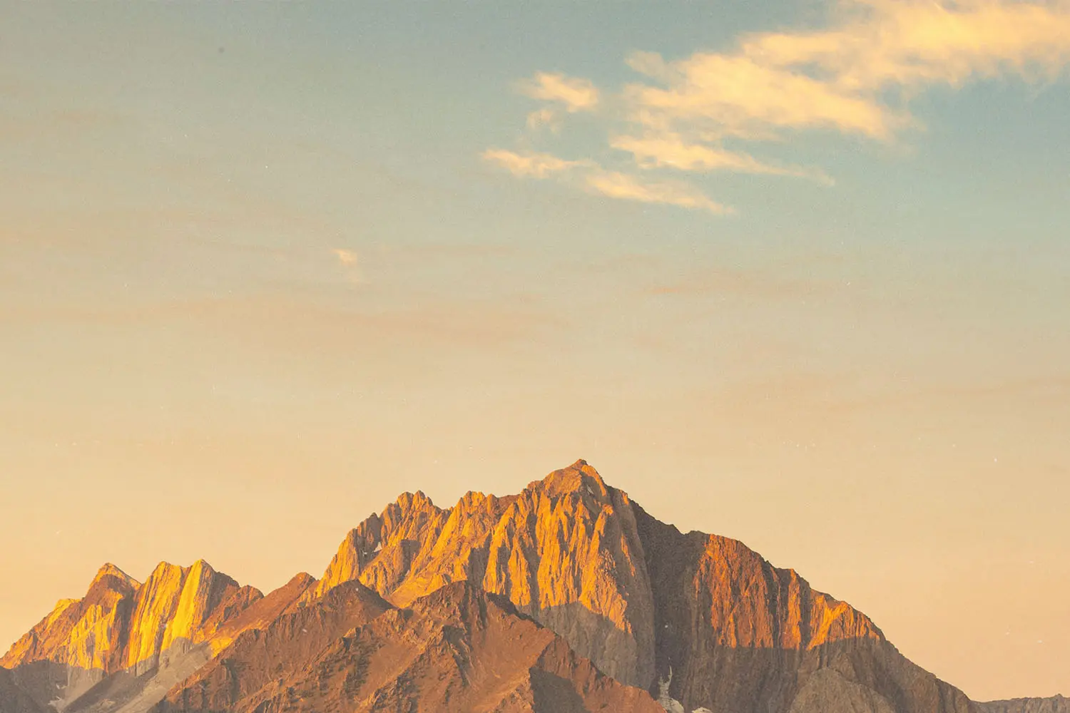 Sunrise casting warm hues across rugged mountain tops under a pale sky