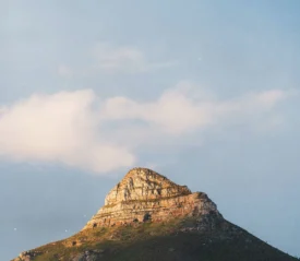 Sunlit rocky mountain peak rising against a soft blue sky with scattered clouds