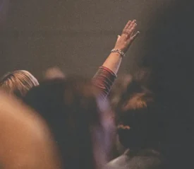 Individual lifting an arm in a crowded indoor space, surrounded by blurred crowd