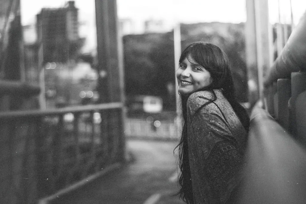 Person standing on a bridge overlooking a city street in a soft, black‑and‑white scene