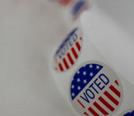A strip of “I Voted” stickers featuring stars and stripes lies on a white surface