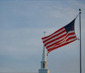 American flag flying on a pole in front of a church steeple