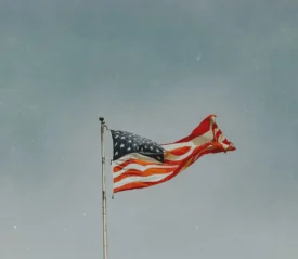 Weathered U.S. flag rippling on a tall pole beneath a cloudy sky