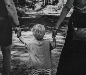 Little boy standing in the middle of his parents while holding their hands