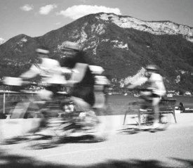 Motion-blurred cyclists moving along a waterfront trail with towering mountains behind them