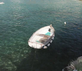 A small white rowboat floats gently on clear turquoise water near a rocky shoreline