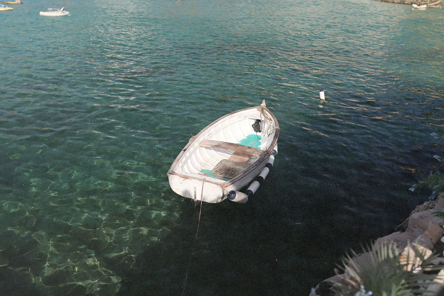 A small white rowboat floats gently on clear turquoise water near a rocky shoreline