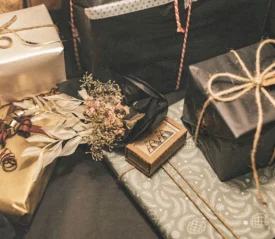 Collection of beautifully wrapped gifts in various decorative papers and twine, accented with dried flowers and festive tags