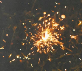 A single sparkler glows brightly in the dark, sending out golden sparks in all directions