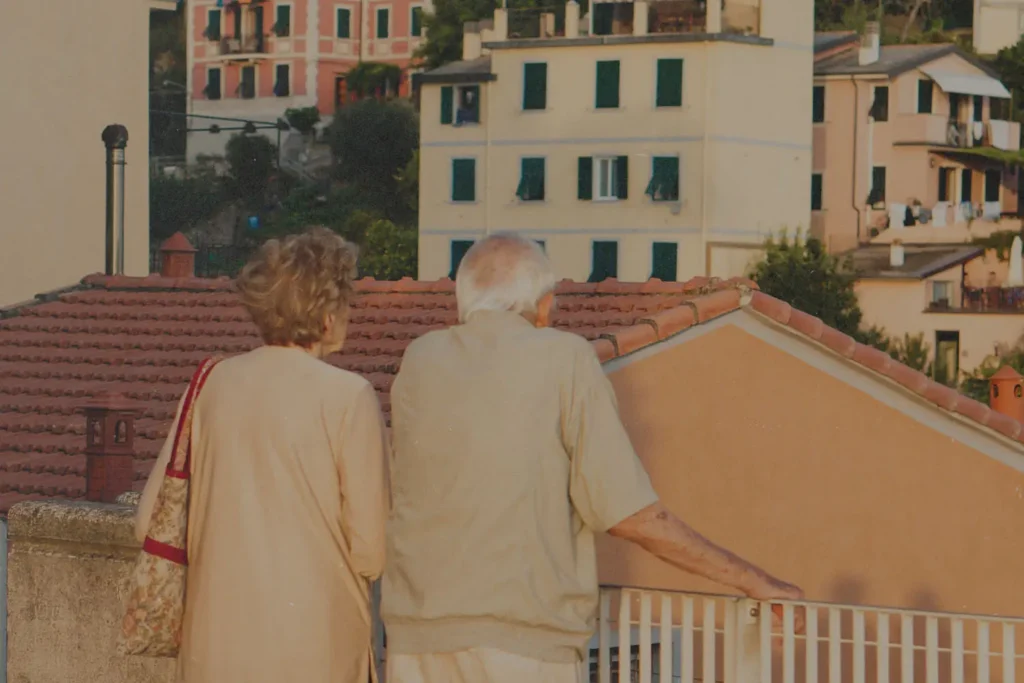 Back of an elderly couple standing on a balcony overlooking city buildings
