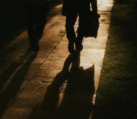 Shadows of two people walking down a dimly lit sidewalk