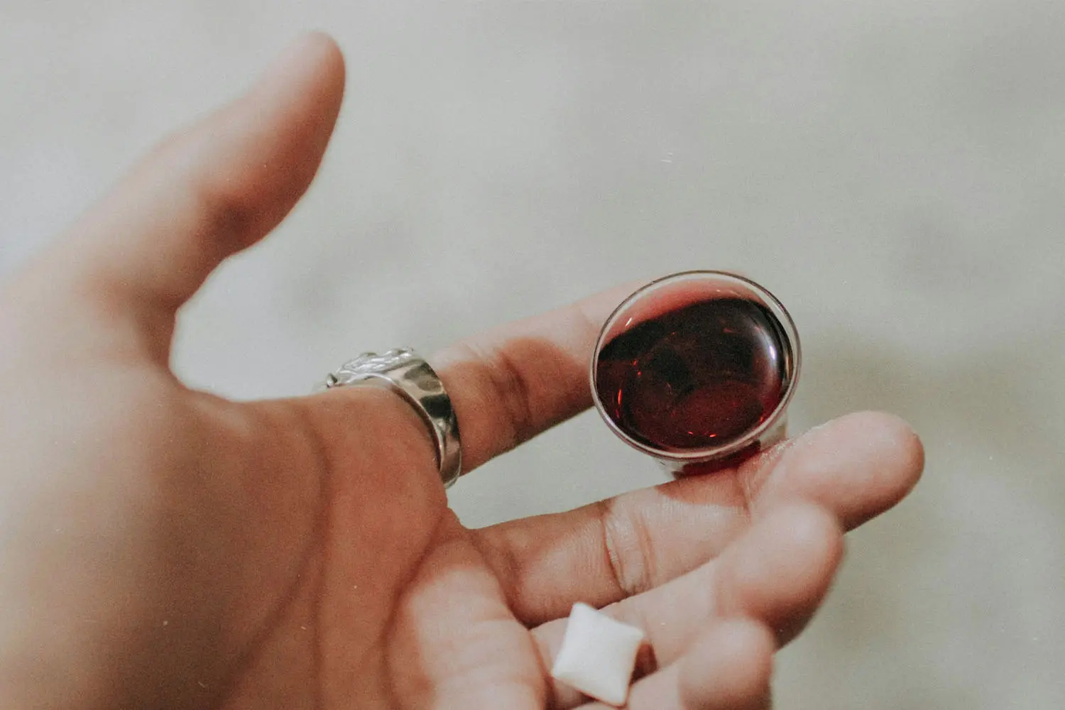 A hand holds a small cup of red communion juice with a white communion wafer resting near the fingertips