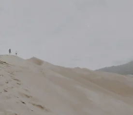 Three people walking up a steep sand dune, leaving footprints in behind