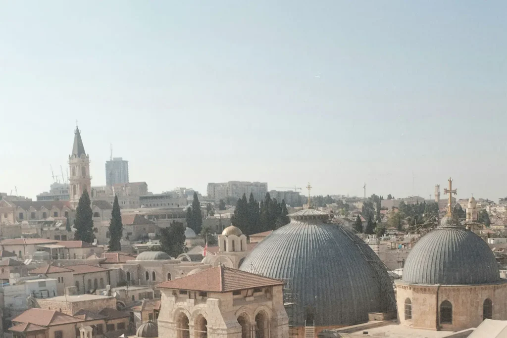 Cityscape featuring domed church roofs, stone buildings, and distant towers under a bright, clear sky