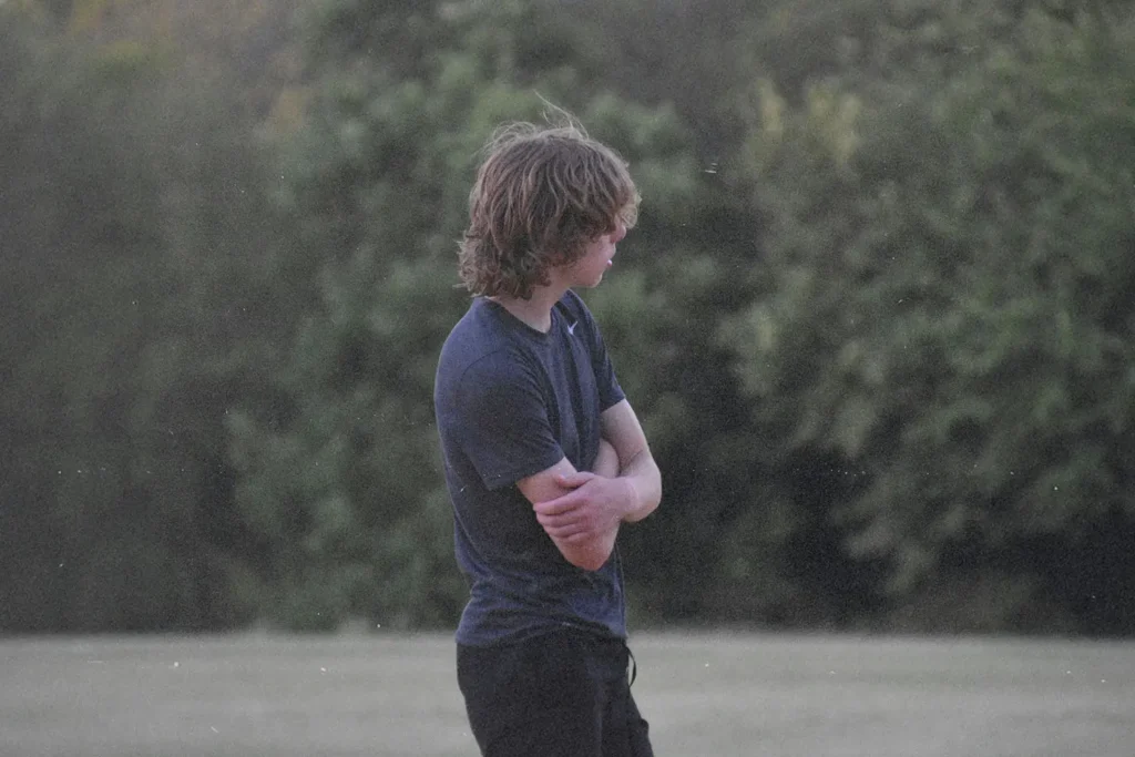 Teenage boy standing hunched with arms crossed looking away from the camera