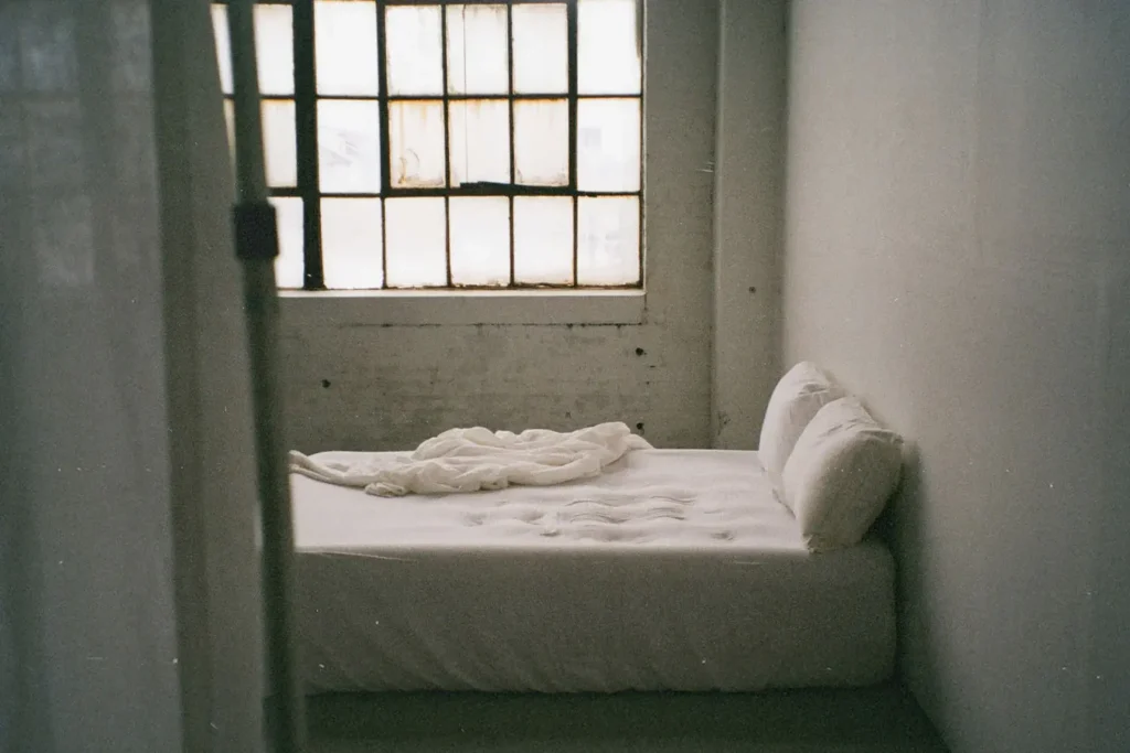 Empty bed with white sheets in a concrete room