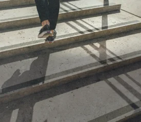 Person walking up concrete steps with sunlight casting long shadows across the staircase