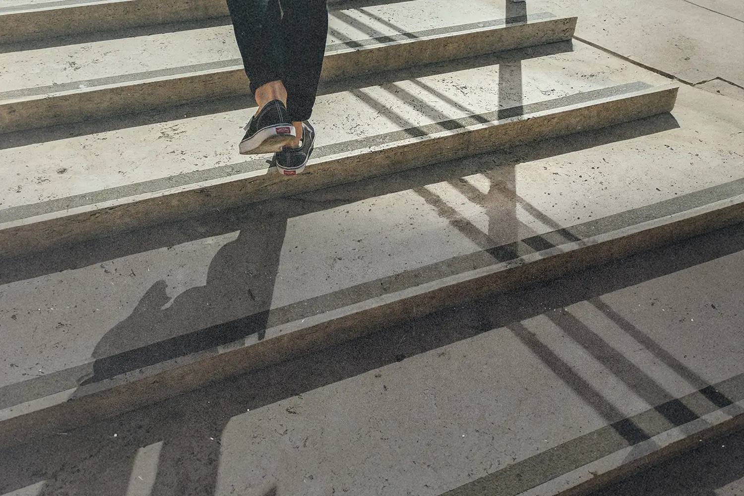 Person walking up concrete steps with sunlight casting long shadows across the staircase