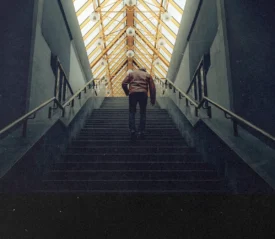 Person walking up a wide staircase inside a building with a geometric glass ceiling overhead
