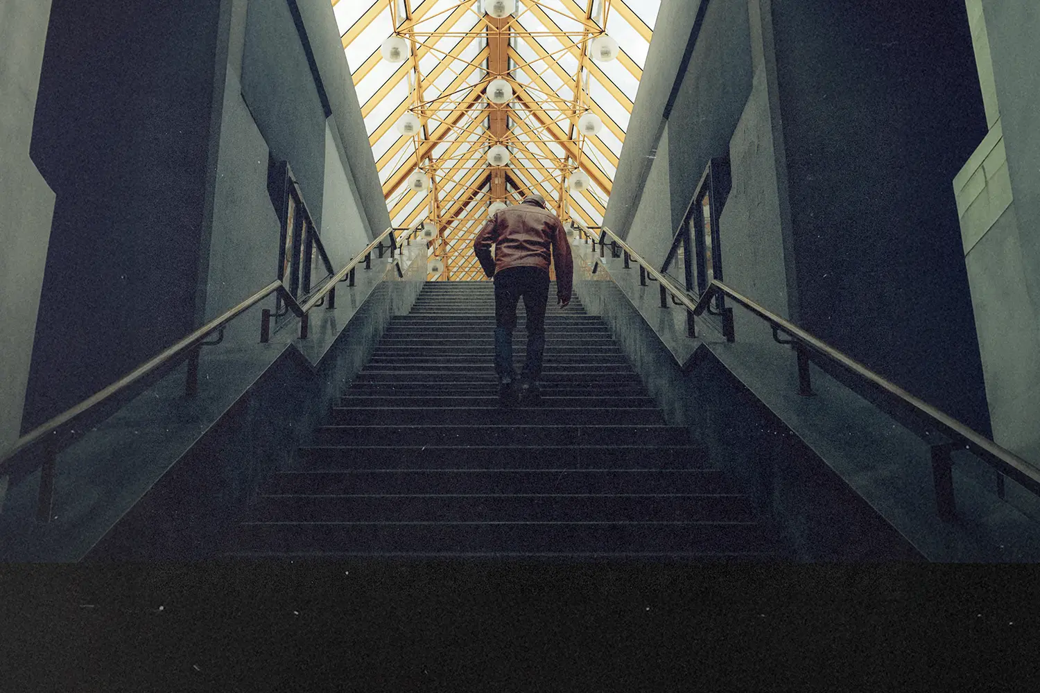 Person walking up a wide staircase inside a building with a geometric glass ceiling overhead