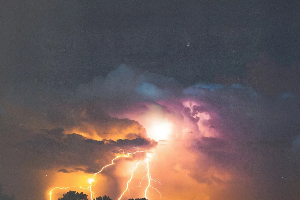 Bright lightning bolts illuminating dark storm clouds with vivid orange and purple tones