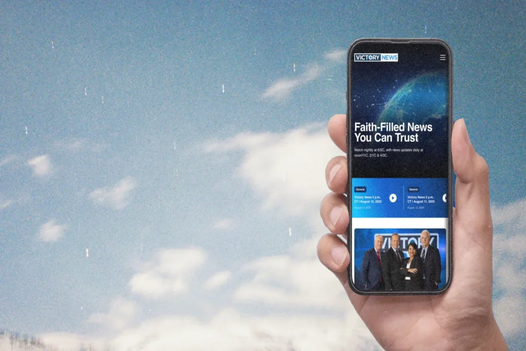 Hand holding an iPhone with the VICTORY News website on the screen