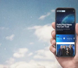Hand holding an iPhone with the VICTORY News website on the screen