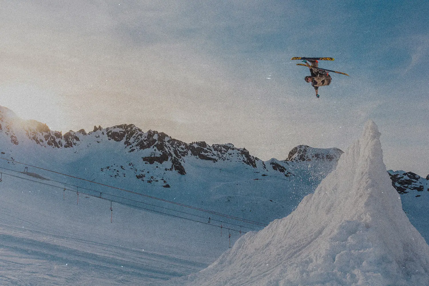 Person performing a midair ski jump above a snowy slope with rugged mountains in the background