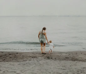 Mother walking on the shore with a child in hand into the sea