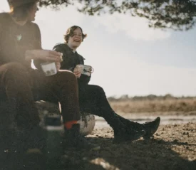 Two people sitting outdoors under a tree, enjoying coffee together as Miracles happen in quiet, natural surroundings.