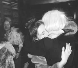 Candid moment of two individuals hugging in a busy room with soft lighting