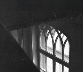 A softly lit arched window seen from above in a dark interior, with faint light shining through the glass panes