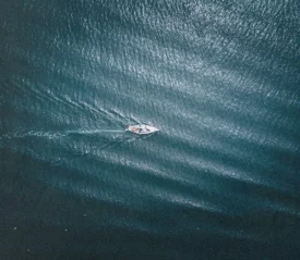“Aerial view of a small boat moving across deep blue water, leaving a soft wake behind it