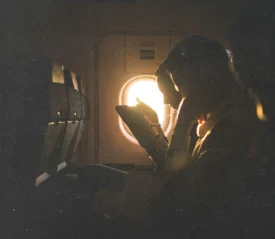 A person sits on an airplane, reading with warm sunlight streaming through the window beside them