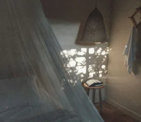 Soft morning light filters through a window, casting patterned shadows onto a small table holding an open book in a calm bedroom