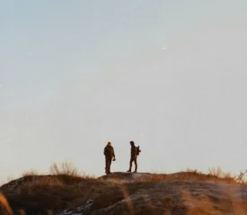 Hikers silhouetted against an open sky while standing on a ridge with dry grass
