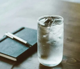 glass of iced water next to black notebook on wood table