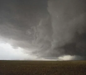Massive storm cloud spreads dramatically across the sky above a flat, open field