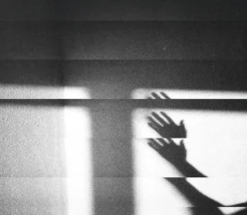 Shadow of raised hands cast across a textured wall in dramatic light and dark bands