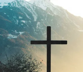 Silhouette of a cross set against sunlit mountains and a soft morning sky
