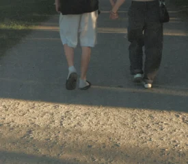 Two people walking hand in hand down a sunlit pathway in a park.