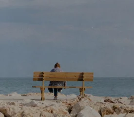 woman sitting alone on a bench on a rocky beach