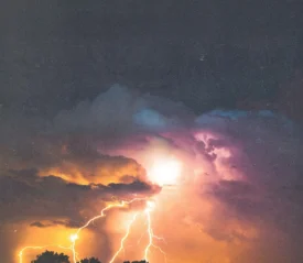 Bright lightning bolts illuminating dark storm clouds with vivid orange and purple tones