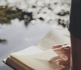 A person holding an open Bible with sunlight shining on the pages.