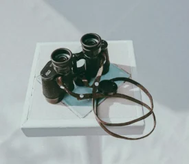 Binoculars and a book on a white table.