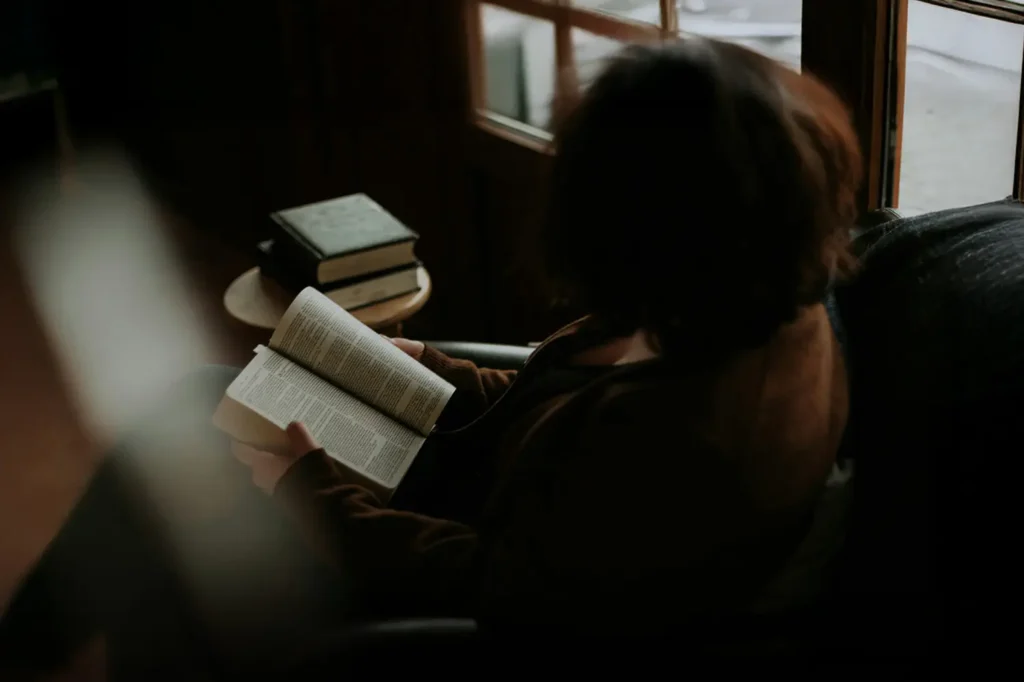 Person sitting by a window reading the Bible in quiet reflection, illustrating intimacy with God through personal fellowship, prayer, and time in God’s presence.