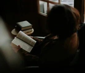 Person sitting by a window reading the Bible in quiet reflection, illustrating intimacy with God through personal fellowship, prayer, and time in God’s presence.