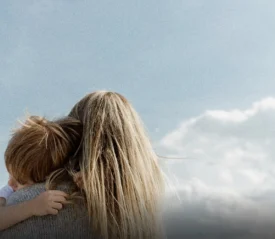 Adult embracing a child outdoors under an open sky, illustrating spiritual motherhood through nurturing presence, guidance, and generational connection.